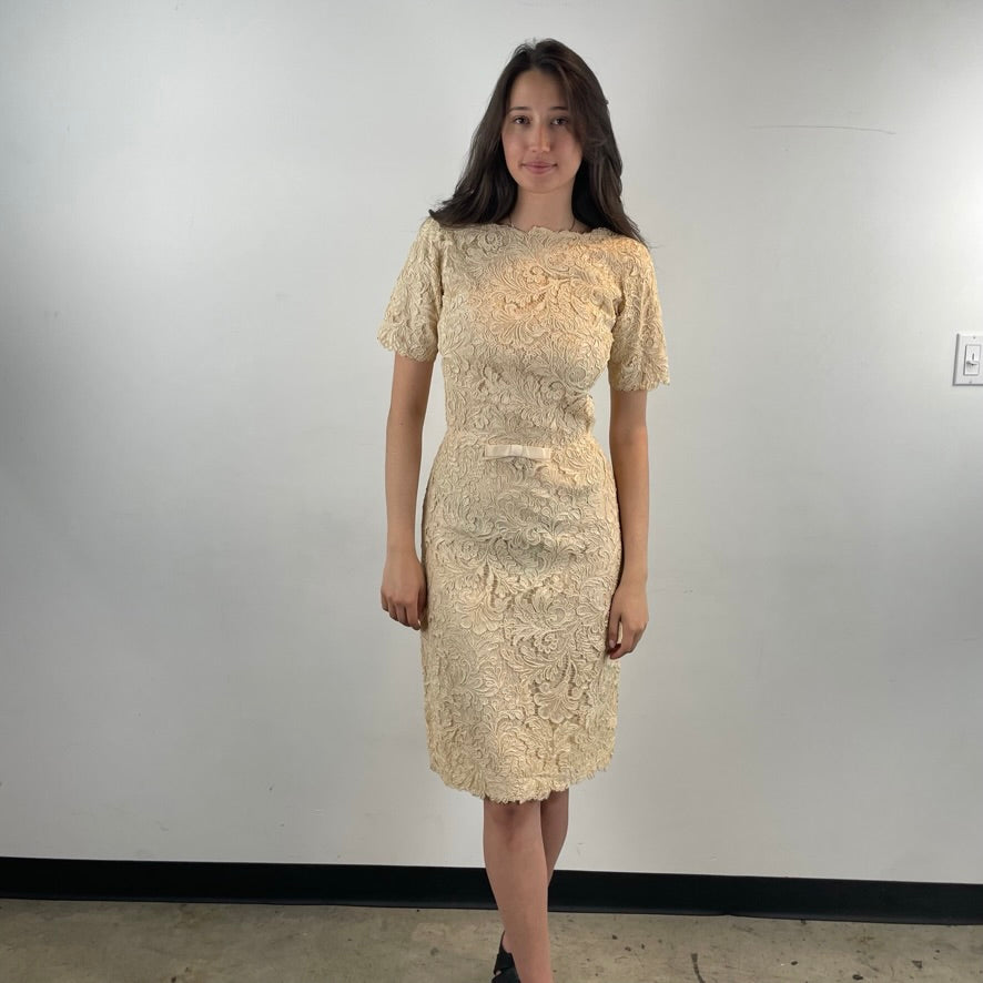 Front View of Boheme Vintage 1960s ivory lace dress with scalloped edges, dolman sleeves, and satin bow waist detail.