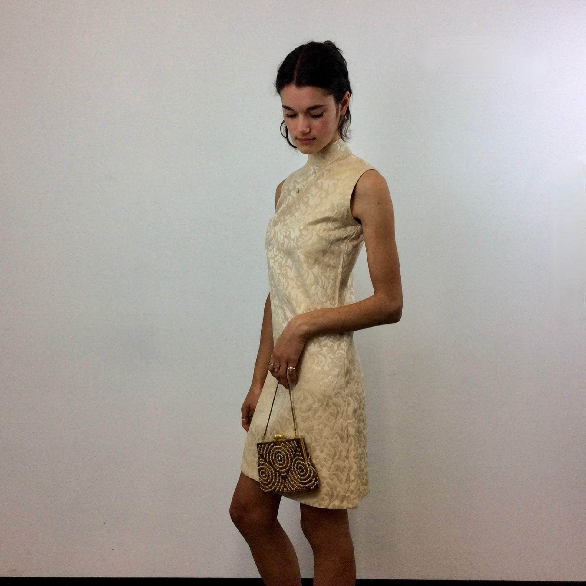 Side view of 1960s Beige Brocade Sleeveless Satin Shift Dress Small. Styled with 1960's Gold Beaded Evening Bag. Sold by Bohème Vintage. Montreal.