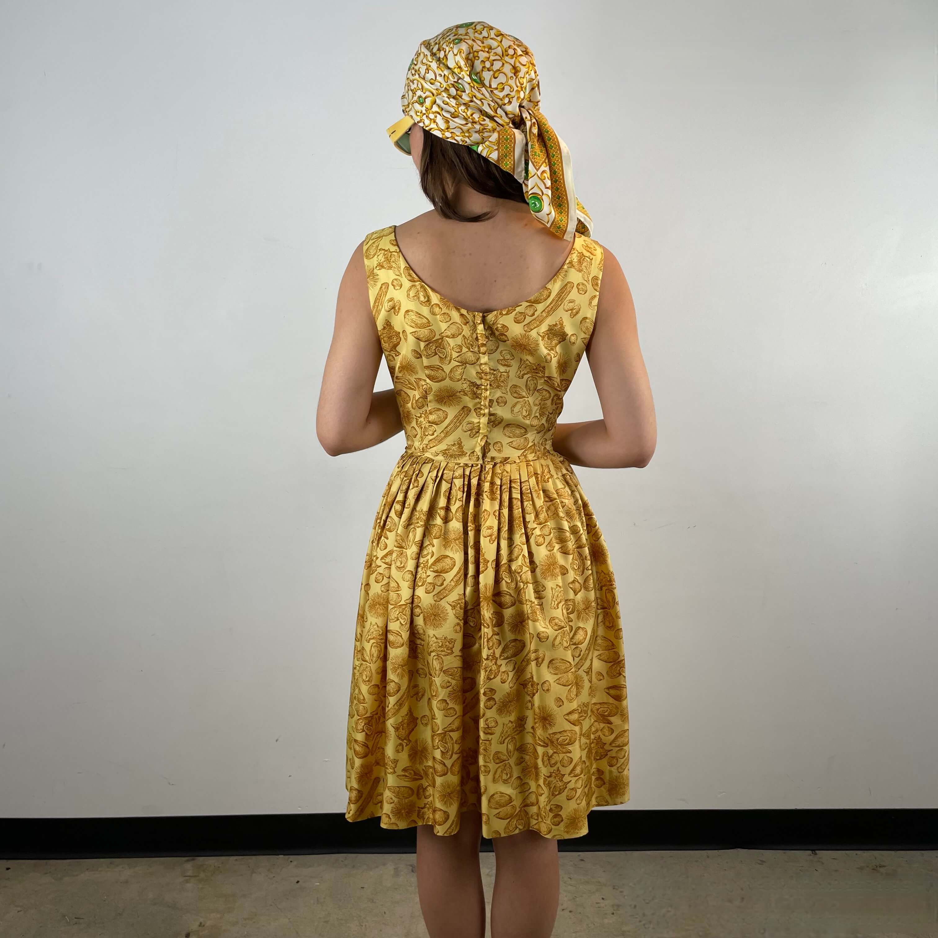 Back view of Boheme Vintage 1950s L’aiglon seashell print gold acetate dress with pleated skirt and fitted bodice.