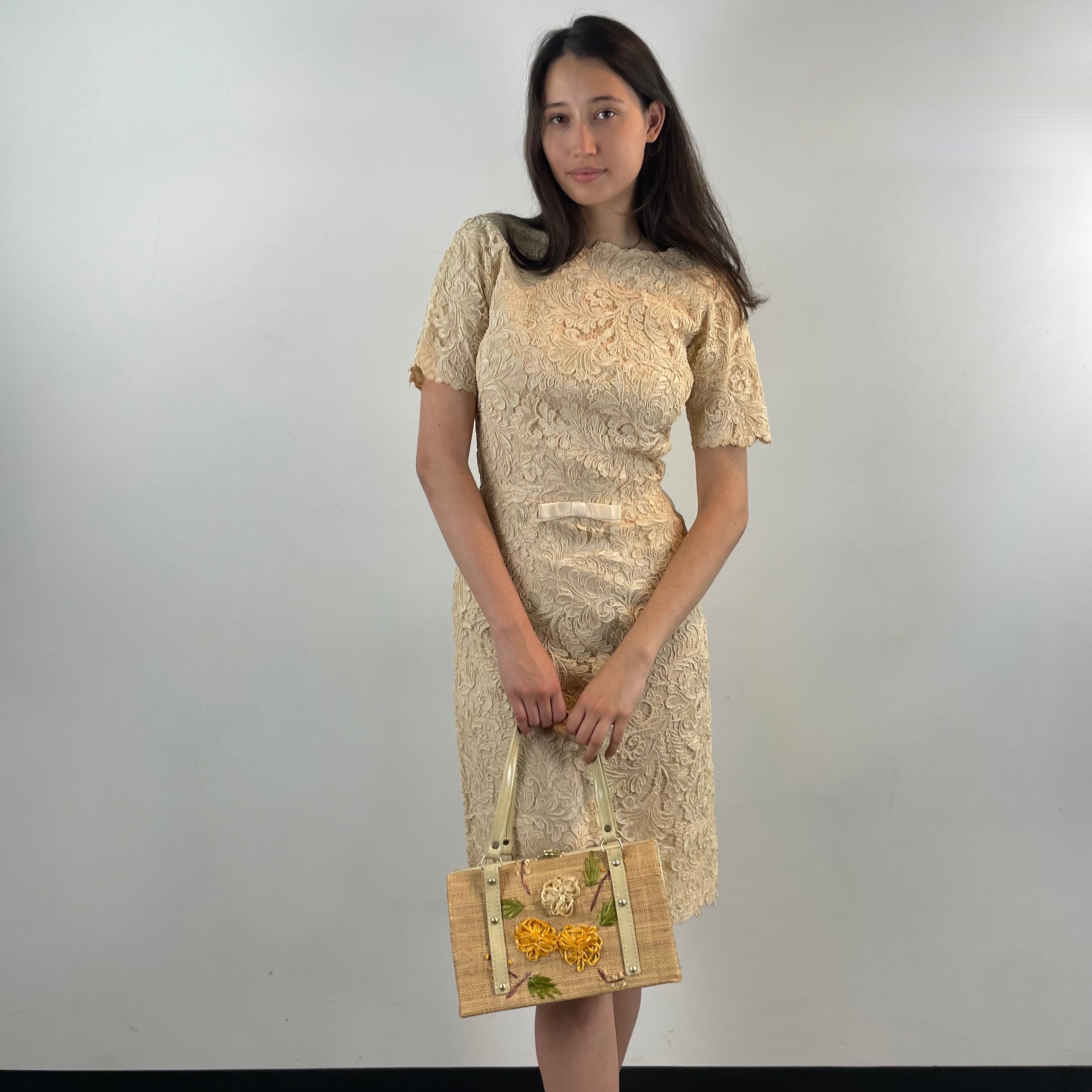 Front View of Boheme Vintage 1960s ivory lace dress with scalloped edges, dolman sleeves, and satin bow waist detail.