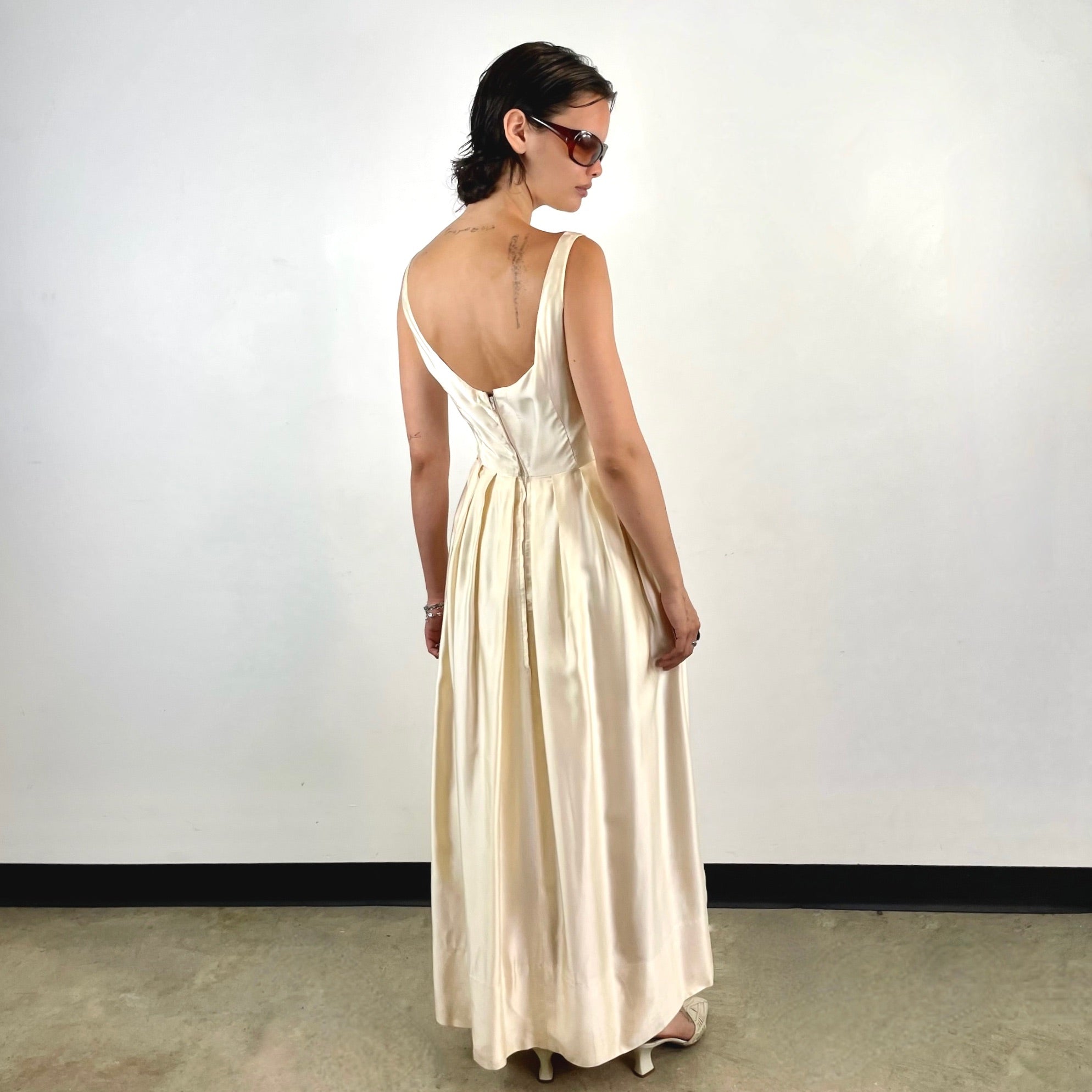 Boheme Vintage 1970s ivory satin gown with open back, pleated skirt, and fitted bodice.