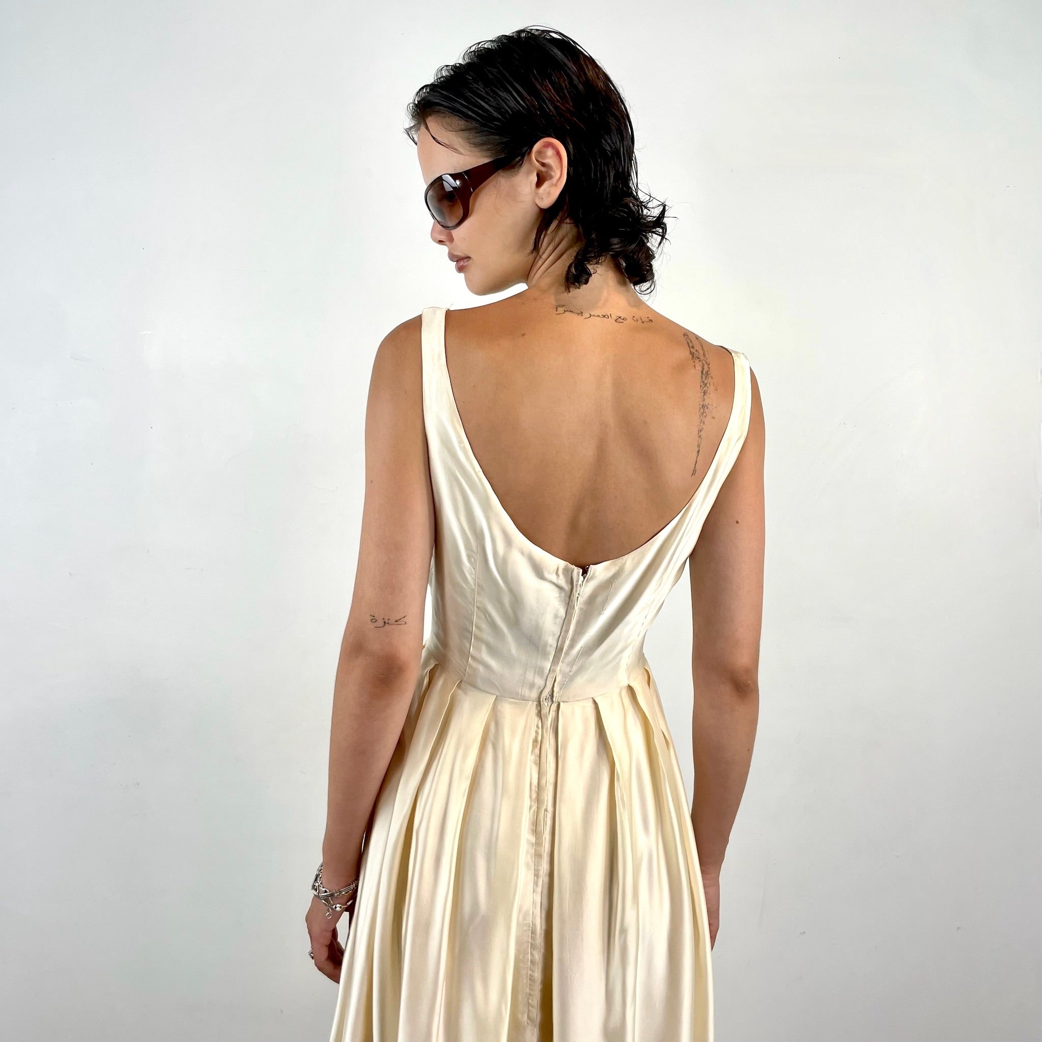 Boheme Vintage 1970s ivory satin gown with open back, pleated skirt, and fitted bodice.